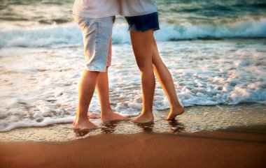 Plajda kot şortlu kadın ve erkek bacakları, akşam romantik bir fotoğraf..