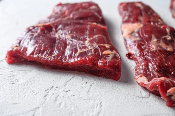 Alternative Flank steak, churrasco beef organic meat cut side view close up over white concrete background.