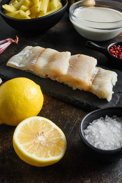 British traditional fish and potato chips ingredients raw fish fillet, beer batter, potatoe, shallotgarlic, salt, peppercorns on rustic metal textured surface or table side view .