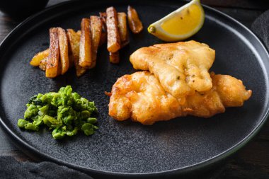 Balık ve patates kızartması. Kızarmış balık, patates cipsi, bezelye püresi ve tartar sosundan oluşan geleneksel İngiliz yemeği. Bar manzaralı eski siyah ahşap masanın üzerinde servis edilir..