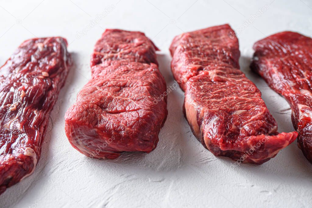 Raw organic denver steak in front of machete denver cuts marble beef on white background