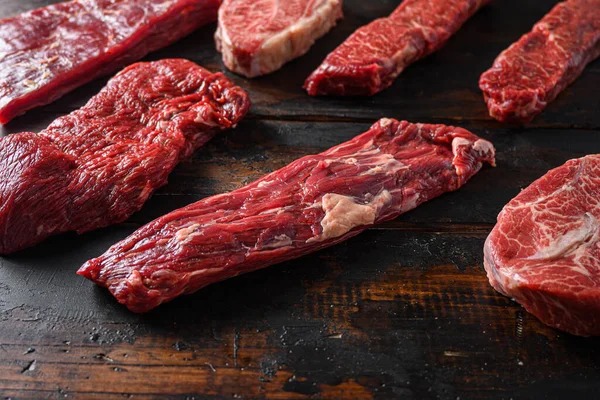 Alternative beef cut machete skirt steak close up in front of other cuts in butchery on old wood table side view selective focus.