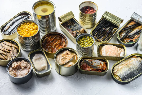 Assortment of canned preserves food in cans, conserve Saury, mackerel, sprats, sardines, pilchard, squid, tuna pinapple, corn, peas, mango , beans, over white textured background side view