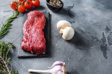 Organik Tri-Tri-Tri, siyah tabakta üçgen kavrulmuş biftek, bitkilerle mermer sığır eti, domates, karabiber, gri taş yüzey arka plan alanı, metin için yeni geniş açı..