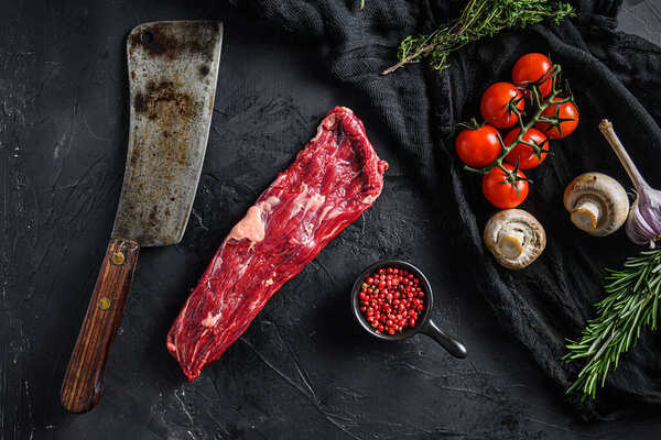 Organic machete or skirt steak near butcher knife with pink pepper and rosemary. Black background. Top view