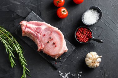 Manzaralı çiğ domuz pirzolası biftek ve tuz, biberiyeli siyah taş tahtada biber ve siyah desenli arka planda ızgara için taze malzemeler..
