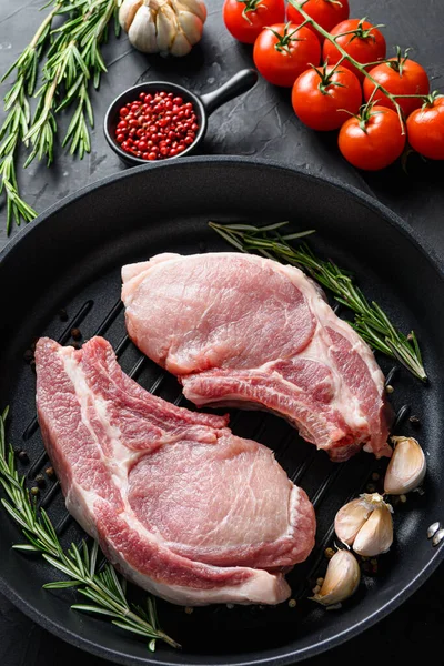 Raw Pork Loin chops in skillet near ingredients wtih herbs pepper and tomatoes top view vertical selective focus noone.