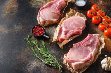 Bitki, yağ ve baharatla sıralanmış çiğ domuz pirzolası. Et pişiriyorum. Metin için alanı olan koyu arkaplanda.