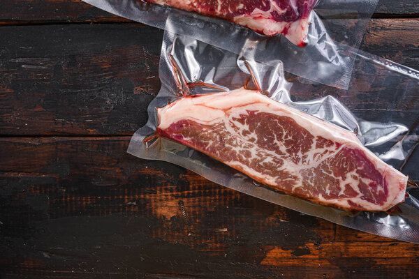 Vacuum packed fresh beef top blade steak for sous vide cooking on dark old wooden background, top view with space for text