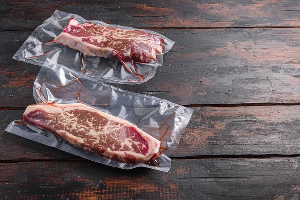 Vacuum packed meat , top blade beef steak on dark old wooden table, side view space for text.