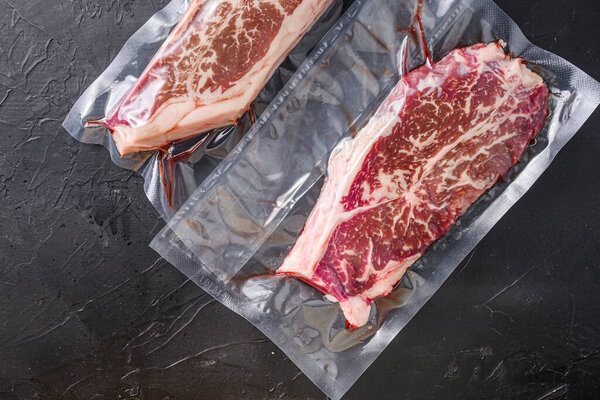 Top blade steak, vacuum packed organic beef for sous vide cooking on black textured background, top view