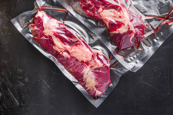 Chuck Tenders beef steak in vacuum sealed bag on black textured background side view