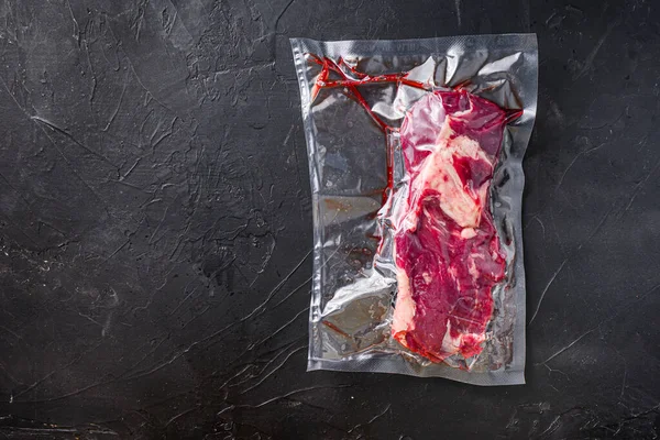 Vacuum packed organic beef chuck roll steak for sous vide cooking on black textured background, top view space for text