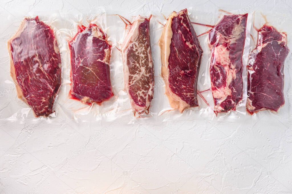 Set of vacuum packed organic raw beef alternative cuts: top blade, rump, picanha, chuck roll steaks, over white background, top view space for text