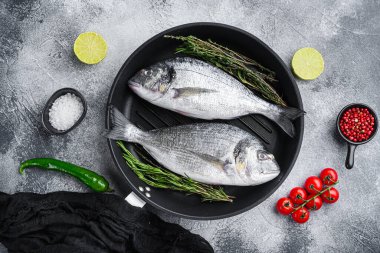 Bir çift deniz kabuğu ya da ızgara tavasında çiğ balık, gri beyaz desenli arka plan, üst görünüm.