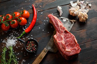 Koyu ahşap masa arkasında çiğ Delmonico bifteği. Baharatlı, biberiyeli, domatesli, chikie 'li, sarımsaklı, biberli, biberli, et bıçağı saplı, tuzlu biftek ya da barbekü. Kapat..