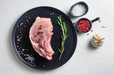 Beyaz bir arka planda siyah yuvarlak bir tabak içinde çiğ domuz filetosu ve ızgara üst görünümü için biberiyeli sarımsaklı biber taneleri..