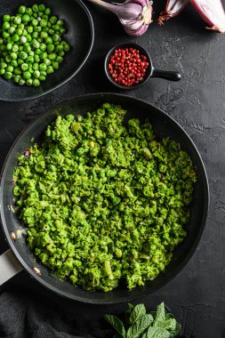 Mushy peas recipe cooked frying pan and peas in bowl with mint shallot pepper and salt on black stone surface  organic keto food top view close up. clipart