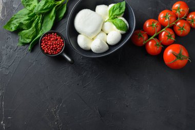 Küçük mozzarella peyniri topları, taze kiraz domatesleri, fesleğen yaprağı, siyah kayrak taşından yapılmış siyah karatahta Caprese salatası için peynir. Üst görünüm.