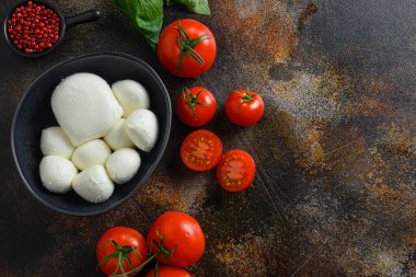 Mozzarella peyniri, kiraz domatesleri ve fesleğen yaprakları koyu rustik metal zemin üzerinde gül biberi, Caprese salatası üst görünümü için İtalyan mutfak malzemeleri. Metin için boşluk.