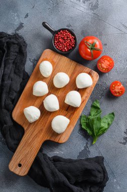 İtalyan Caprese salatasının içeriği olan taze fesleğen yapraklı ve kiraz domatesli bufalo Mozzarella peynir topları siyah bir bez ve gri beton arka plan dikey üst görünüm üzerinde..