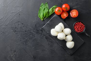 Taze kiraz domatesleri, fesleğen yaprağı, siyah tahta üzerinde mozzarella peyniri sağlıklı İtalyan geleneksel Caprese salatası malzemeleri. Organik Akdeniz gıda kavramı, metin yatay üst görünümü için alan.