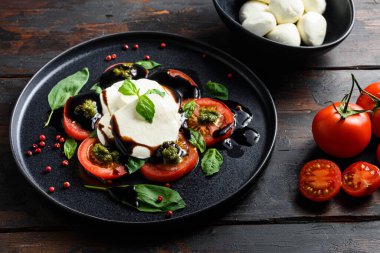 Siyah tabak kiraz domatesli Caprese salatası, mozzarella peyniri, fesleğen, pesto sosu. Kapat, eski ahşap arka plan