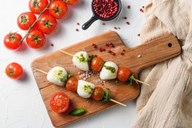 Çubuklarda Caprese salatası, Cherry domatesleri, mozzarella peyniri, fesleğen, ahşap tahtada pesto sosu beyaz kırsal arka plan manzarası.
