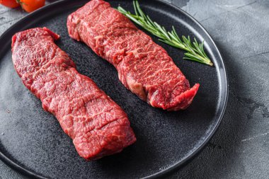 Siyah tabakta organik Denver bifteği, otlu mermer sığır eti, domates, karabiber, gri taş zemin üzerinde karabiber. Arka plan görünümü metin için seçici odak alanını kapat.