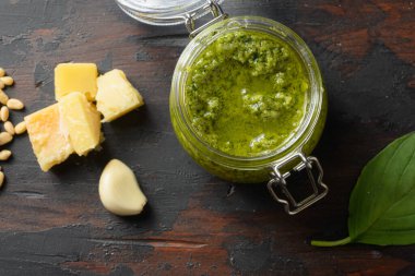İçinde parmesan fesleğen ve çam fıstığı bulunan cam kavanozda pesto alla Genovese. Koyu ahşap masa tahtalarının üzerinde..
