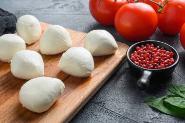 İtalyan Caprese salatasının içeriği olan taze fesleğen yapraklı ve kiraz domatesli bufalo Mozzarella peynir topları siyah bir bez ve gri beton arka planda..