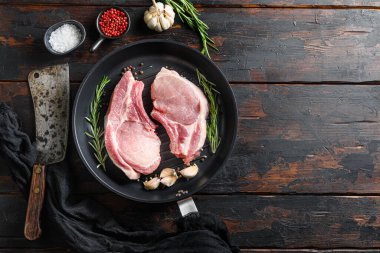 Köhne ahşap mutfak masasında, ızgara için biberiyeli sarımsaklı biberli ve kasap bıçağıyla fotokopi makineli üst görüşü olan domuz pirzolası rostosu.