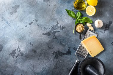 İtalyan pesto için farklı malzemeler. Parmesan peyniri, fesleğen yaprağı, çam fıstığı, zeytin yağı, sarımsak, tuz ve biber harcı ile birlikte koyu arka planda pişirilen taştan masa malzemeleri. Boş metin alanı olan bir düzen