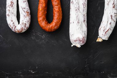 İspanyol salamı, fuet ve Chorizo sosisleri siyah yüzey üzerinde asılı fotokopi alanı ile.