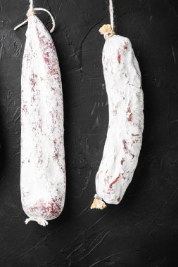 İspanyol salamı, fuet ve sucuk sosisleri siyah arka planda asılı duruyor..