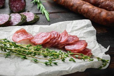 Koyu ahşap arka planda otlarla dilimlenmiş kurutulmuş sucuk, fuet ve diğer sosisler..