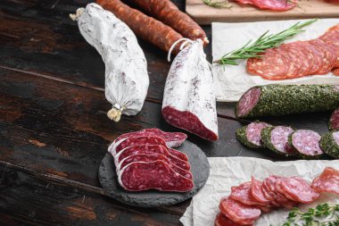 Koyu ahşap arka planda otlarla dilimlenmiş kurutulmuş sucuk, fuet ve diğer sosisler..