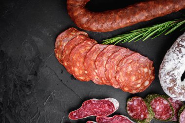 Kurumuş salam seti, İspanyol sosisi, dilimler ve kesikler siyah desenli yüzey, üst görünüm.