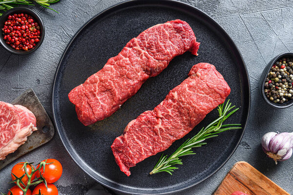 Raw set of denver steaks ob black plate raw organic food , marbled beef with herbs tomatoes peppercorns over grey stone surface background  top view