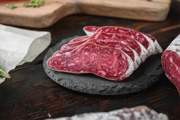 Koyu ahşap arka planda otlarla dilimlenmiş kurutulmuş sucuk, fuet ve diğer sosisler..