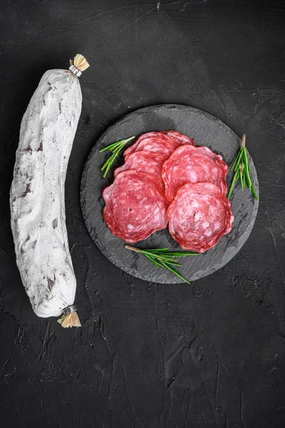 Kurumuş, bütün ve dilimlenmiş siyah arka planda salchichon sosisi, düz uzanmış.