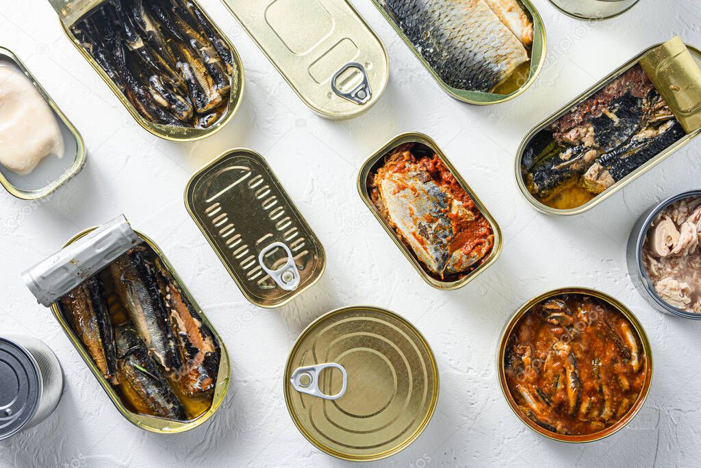 opened cans with different types of fish and seafood, opened and closed cans with Saury, mackerel, sprats, sardines, pilchard, squid, tuna,  over white stone surface top view.