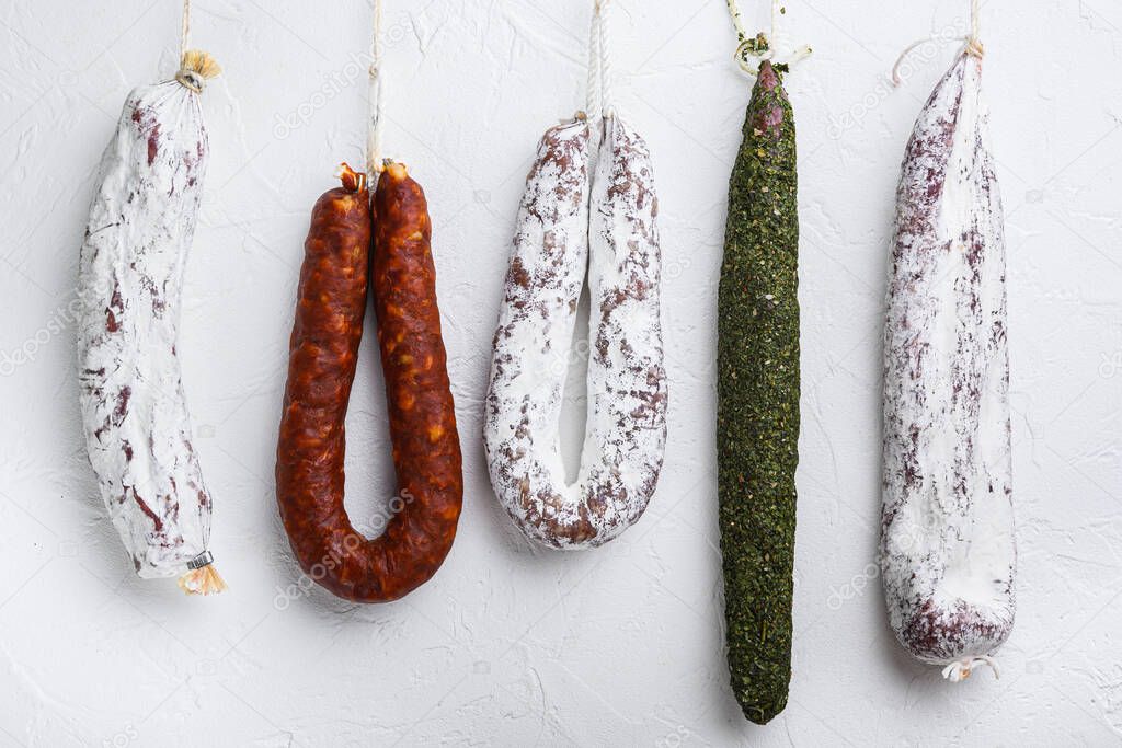 Traditional dry cured sausages meat hanging on white textured background.
