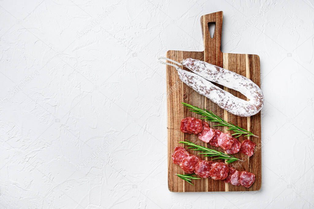 Fuet whole and sliced cuts, spanish dry cured sausage on white surface, flat lay with copy space.
