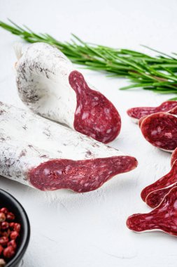 Dilimlenmiş longaniza, kurutulmuş İspanyol sosisi beyaz yüzeyde otlar ve baharatlarla..