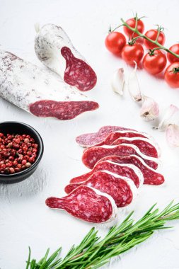 Dilimlenmiş longaniza, kurutulmuş İspanyol sosisi beyaz yüzeyde otlar ve baharatlarla..