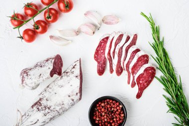 Dilimlenmiş Longaniza dilimleri, kurutulmuş İspanyol sosisi beyaz yüzeyde otlar ve baharatlar, üst görünüm..