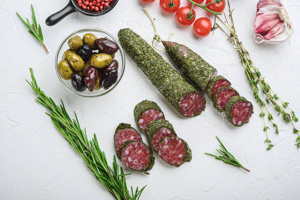 Traditianal fuet sausage in herbs with ingredients on white textured background, topview.
