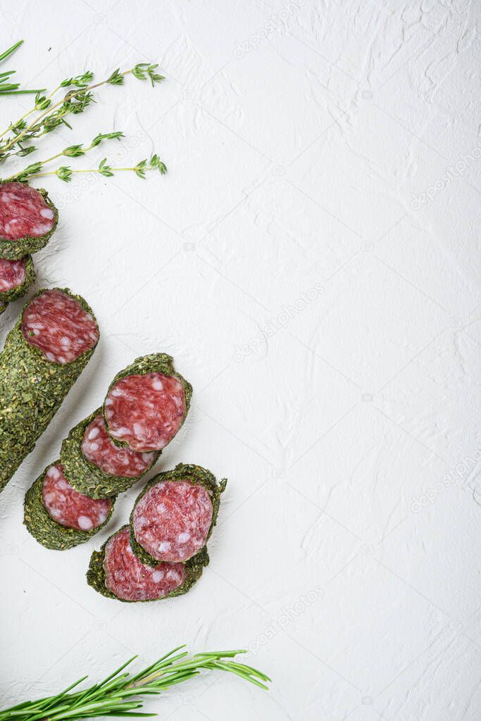 Traditianal fuet sausage in herbs with ingredients on white surface, flat lay with copy space.