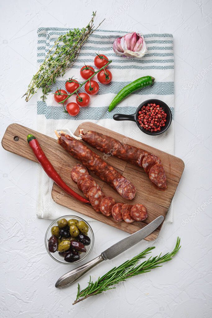 Traditional chorizo cuts with spices and ingredients on white textured background, topview.